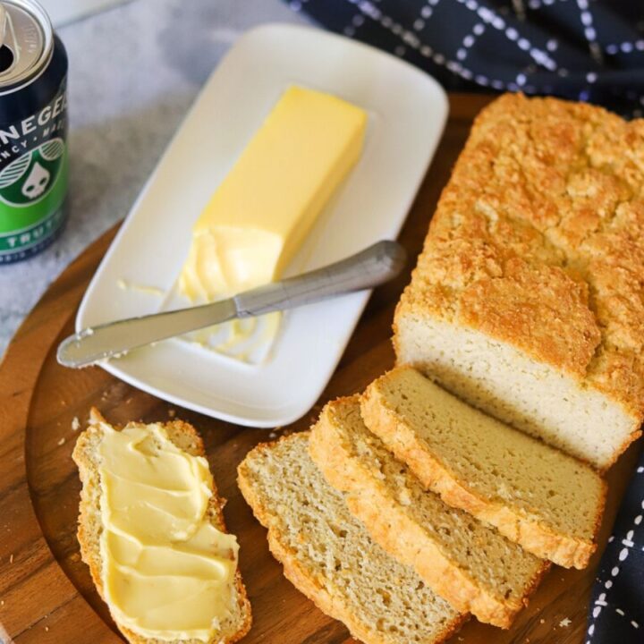Keto bread sliced on a wooden board with a can of beer and butter in the background