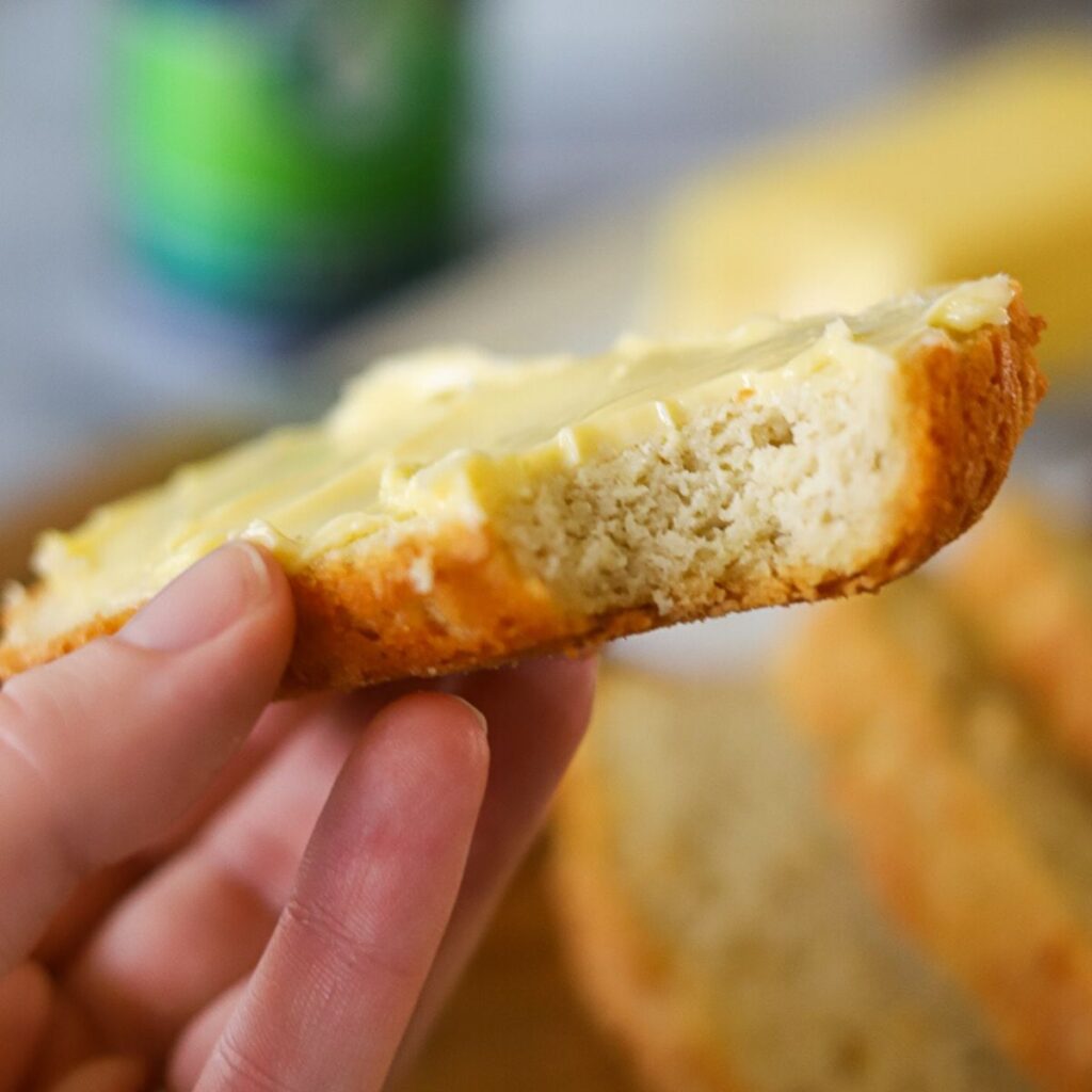 a single slice of low carb beer bread being held up with one bite taken