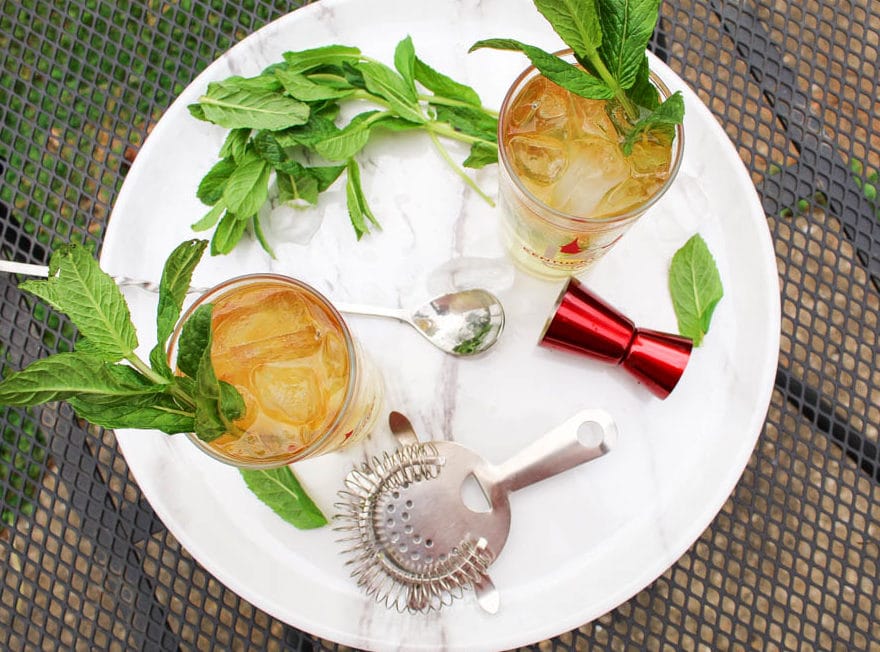 Overhead image of 2 mint juleps with   fresh mint, a cocktail strainer and a jigger 