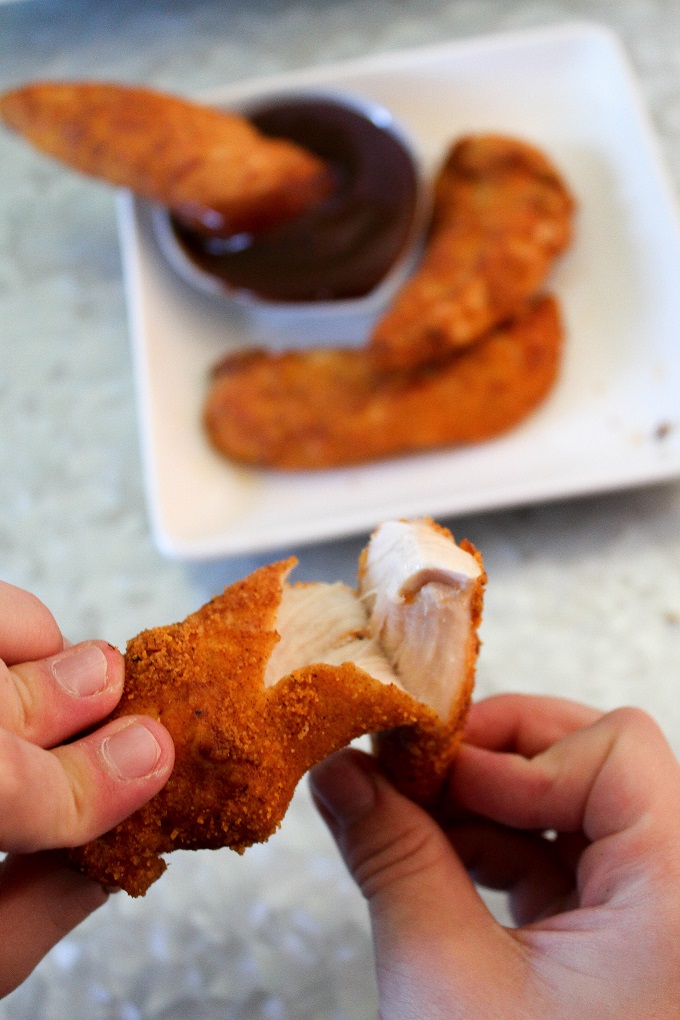 a chicken tender being pulled apart by a child's hands.