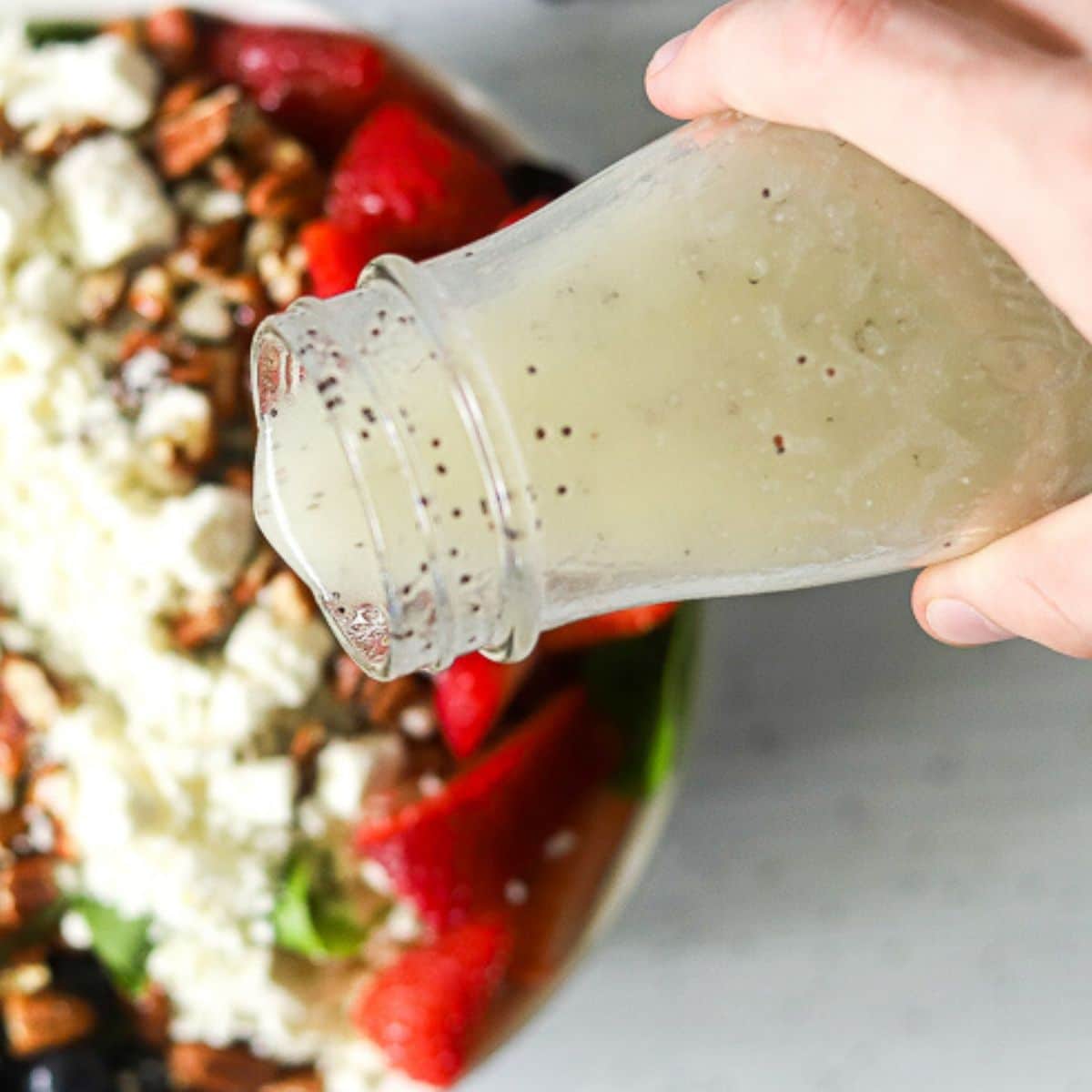 low carb poppyseed dressing being poured over a spinach and strawberry salad