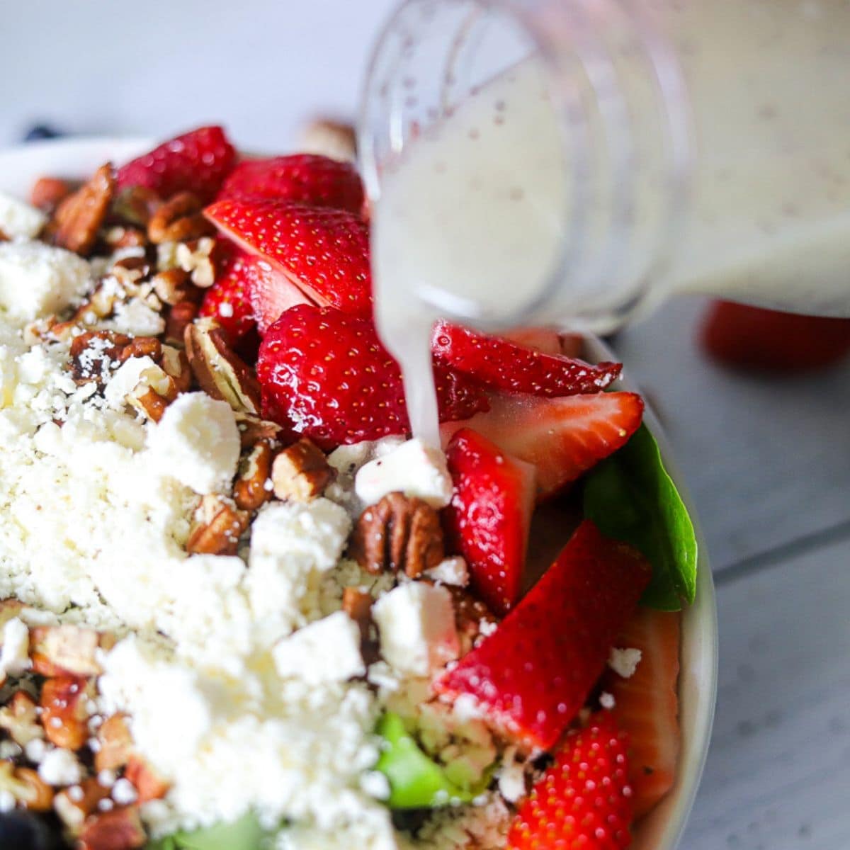 a white bowl full of a low carb strawberry salad with poppyseed dressing being poured on top