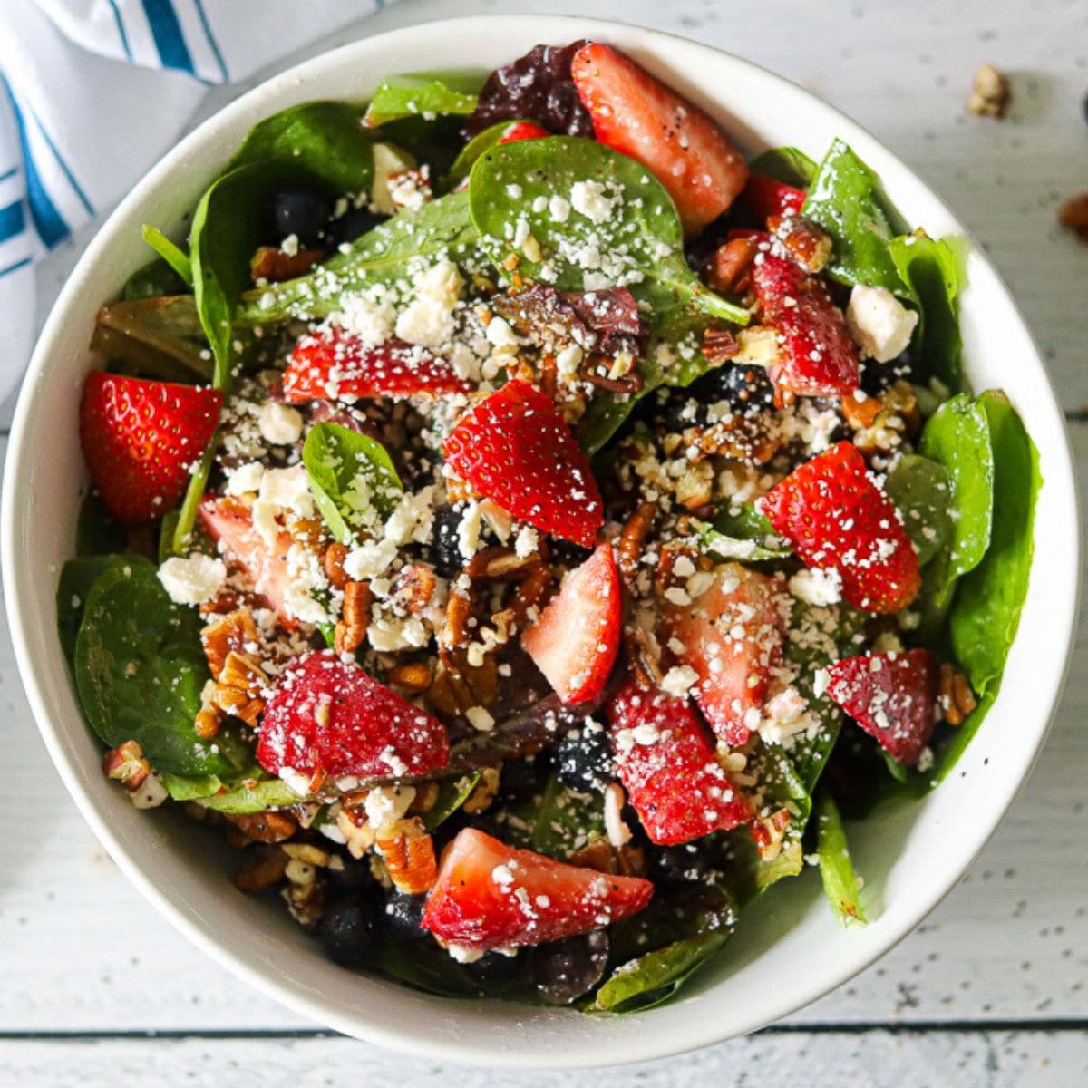 a large white bowl full of lettuxe, strawberries, pecans, blueberries, and feta cheese,