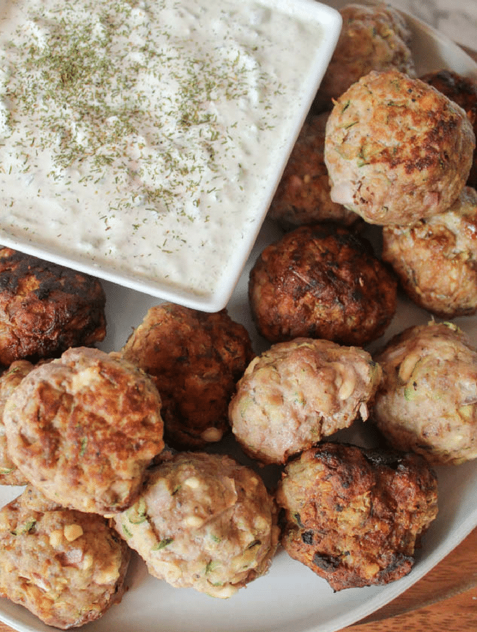 a plate full of Greek meatballs with a square dish of tzatziki in the corner