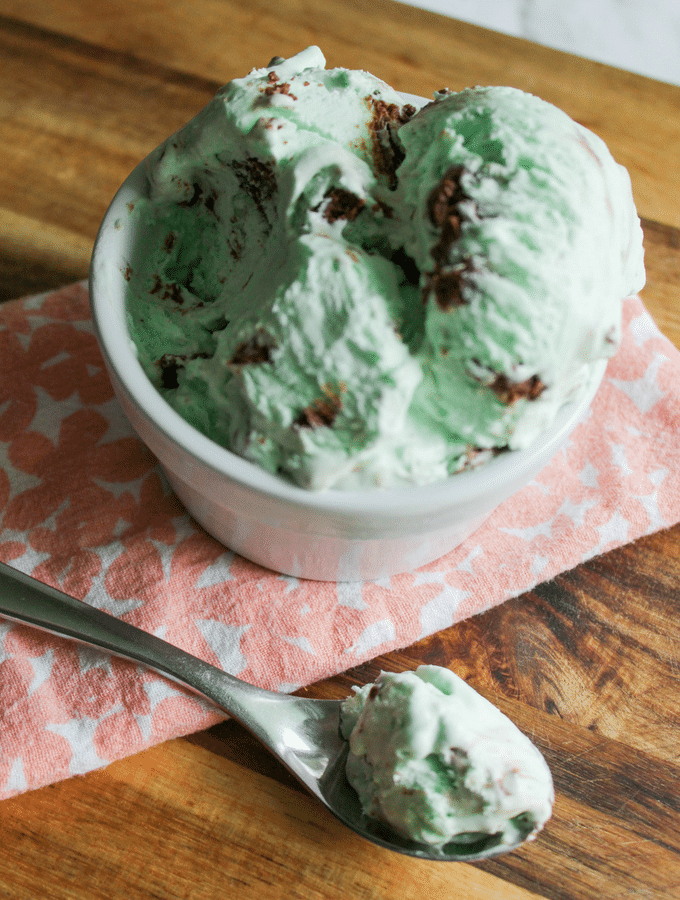 white bowl full of mint chocolate chip ice cream, sitting on a pink floral napkin with a spoonful of ice cream.