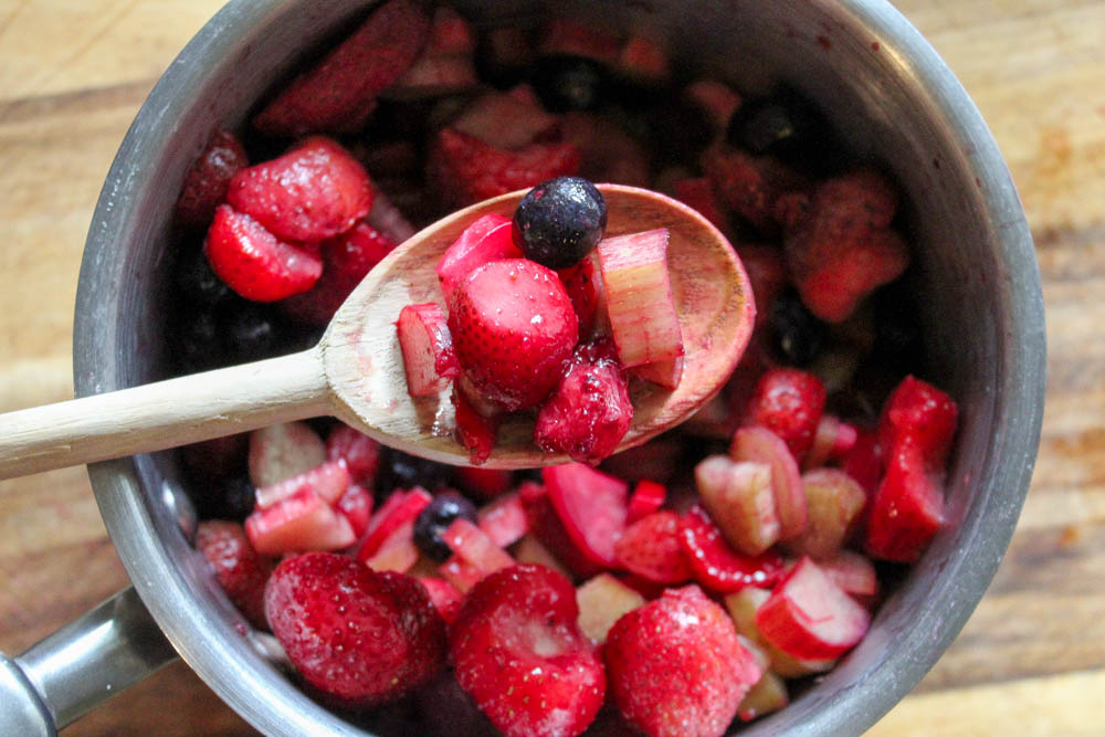 A silver pan full of bluberries, strawberries and sliced rhubarb with a wooden spoon.