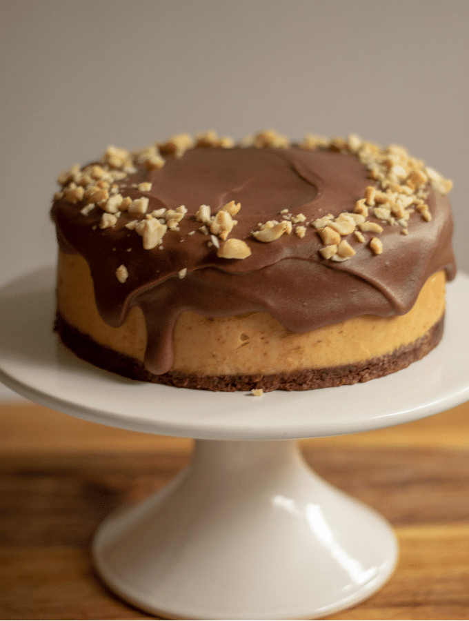 Keto chocolate peanut butter cheesecake on white cake stand