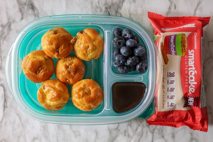 a three compartment food container filled with keto sausage pancake muffins, blueberries, and maple syrup with a pack of smart cakes to the side.