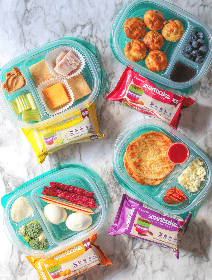Four divided food storage containers full of various keto lunch ingredients and 4 packages of smart cakes. 