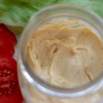 A small mason jar full of bacon mayonnaise with lettuce and tomato off to the side.