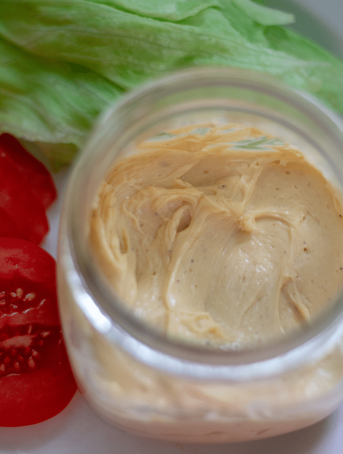A small mason jar full of bacon mayonnaise with lettuce and tomato off to the side.