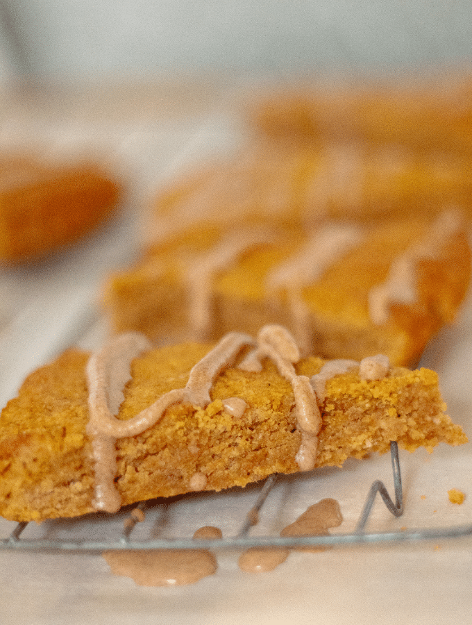 Keto pumpkin scones in a row on a baking rack, being drizzled with a glaze