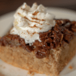 a square slice of upside down maple pecan cake topped with whipped cream, sitting on a round white plate.