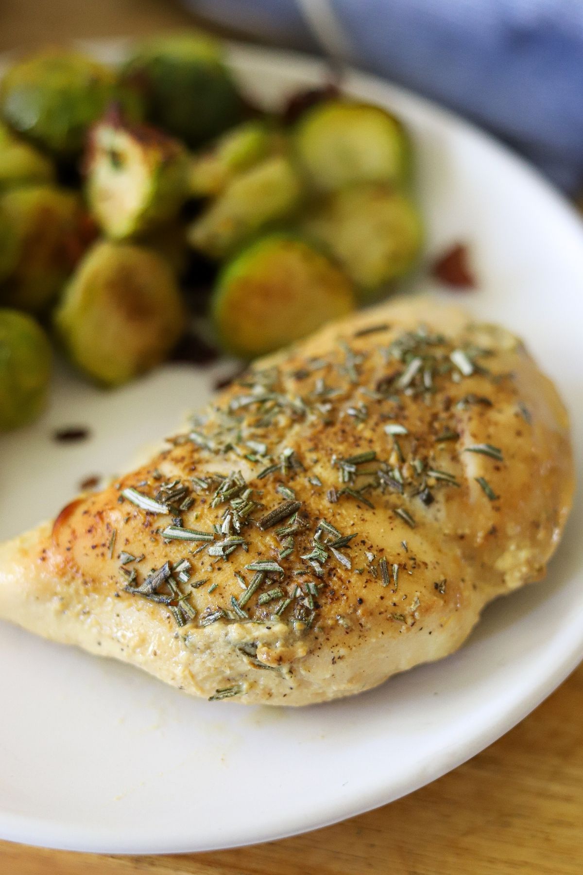 baked chicken topped with maple dijon sauce and fresh chopped rosemary on a plate with brussels sprouts