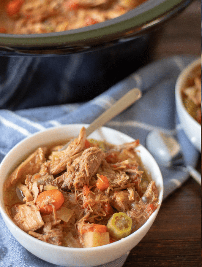 A white bowl full of low carb kentucky burgoo with a slow cooker in the background
