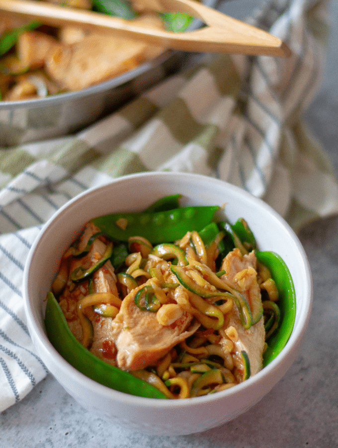 Keto kung pao spaghetti, with chicken, peanuts, zoodles and snow peas in a white bowl.