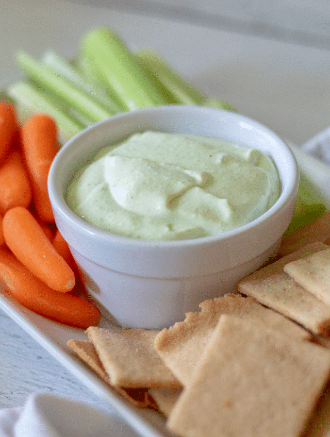 A White platter with a bowl of benedictine in the center surrounded by keto crackers, carrots and celery sticks.