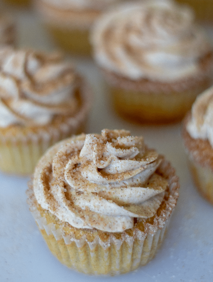 A row of keto cupcakes topped with cinnamon cream cheese frosting and a cinnamon sugar sprinkle