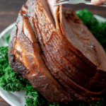 A large, Sugar Free spiral sliced ham on a serving platter surrounded by greenery