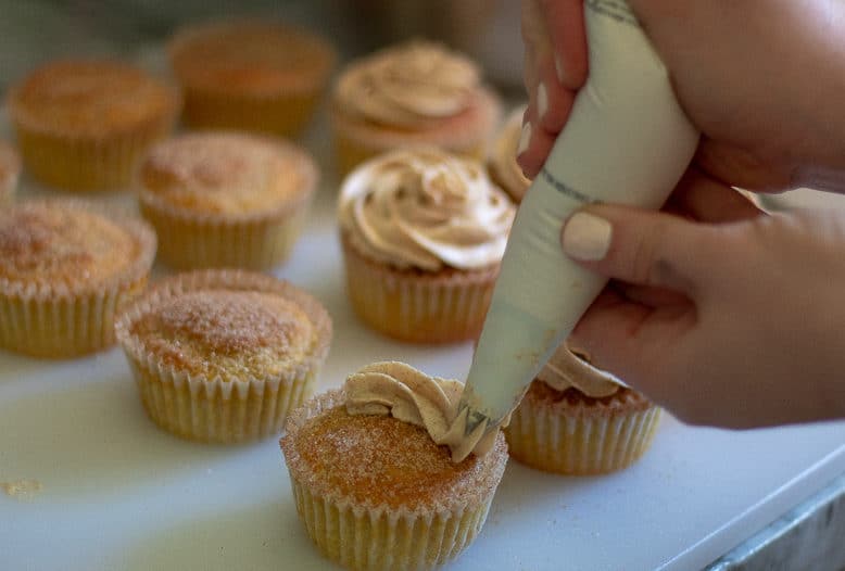 a row of cupcakes with cinnamon cream cheese frosting getting piped on