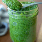 small mason jar full of homemade low carb pesto with a silver spoon full of pesto balanced on top