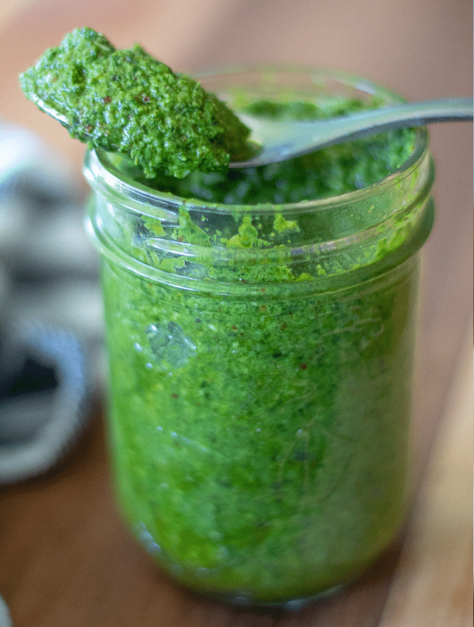 small mason jar full of homemade low carb pesto with a silver spoon full of pesto balanced on top