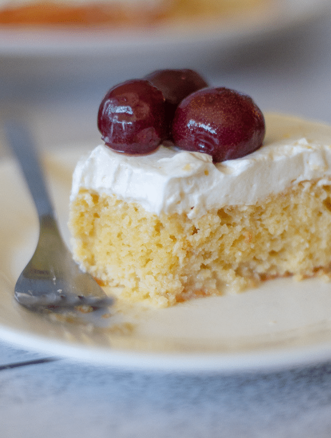 a slice of gluten free tres leches topped with fresh cherries