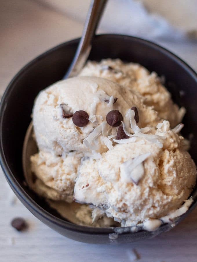 Keto coconut chip ice cream in a black bowl topped with chocolate chips and coconut flakes