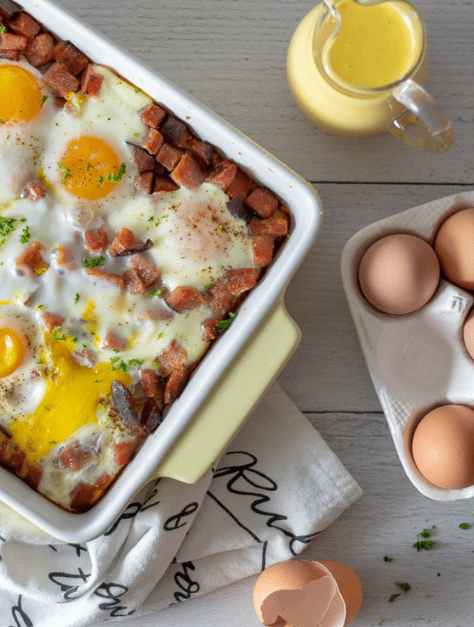 an overhead photo of keto eggs benedict casserole with brown eggs off to the side