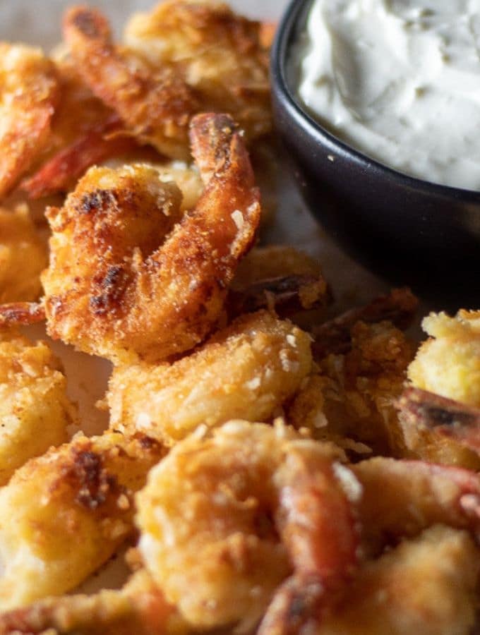 golden and crispy keto coconut shrimp on a white plate with a bowl of pina colada dipping sauce on the side