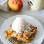 a slice of keto peach cobbler on a white plate topped with vanilla ice cream