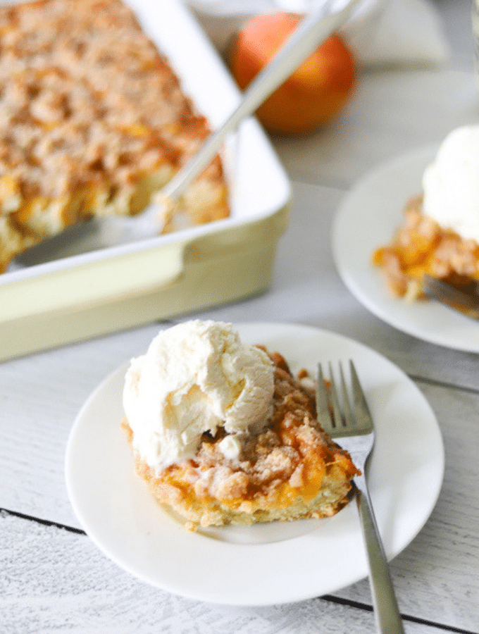 a slice of keto peach cobbler on a white plate topped with vanilla ice cream