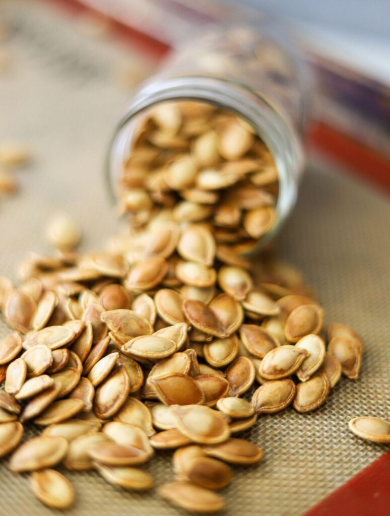 A glass mason jar on its side, overflowing with golden brown roasted pumpkin seeds