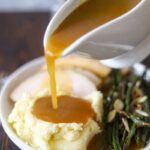 gravy in a boat pouring onto mashed cauliflower