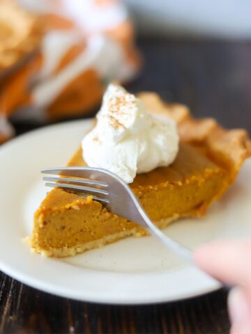 a slice of low carb pumpkin pie topped with homemade whipped cream and cinnamon on a white plate