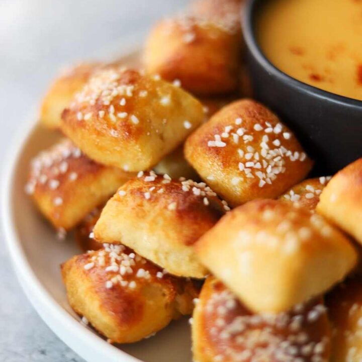 A plate of soft pretzel bites surrounding a bowl of cheese dip
