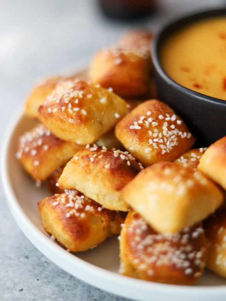 A plate of soft pretzel bites surrounding a bowl of cheese dip