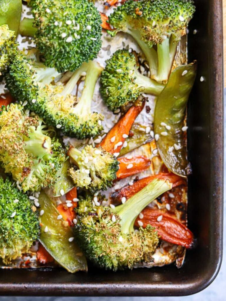 a sheet pan with roasted broccoli, carrots, and snow peas topped with sesame seeds