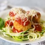 Chicken parmesan meatballs over a bed of zucchini noodles and topped with marinara and cheese