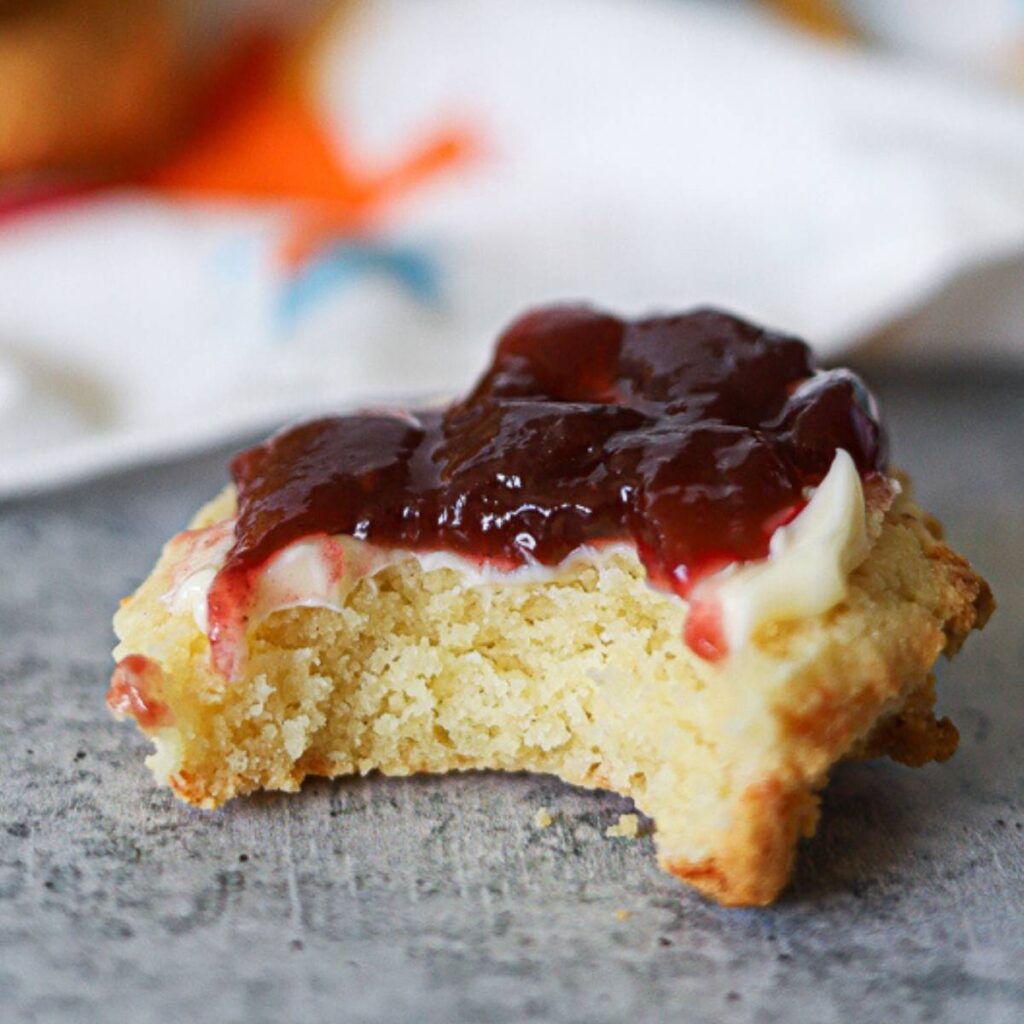 a close of of a biscuit smeared with butter and jam with one bite taken