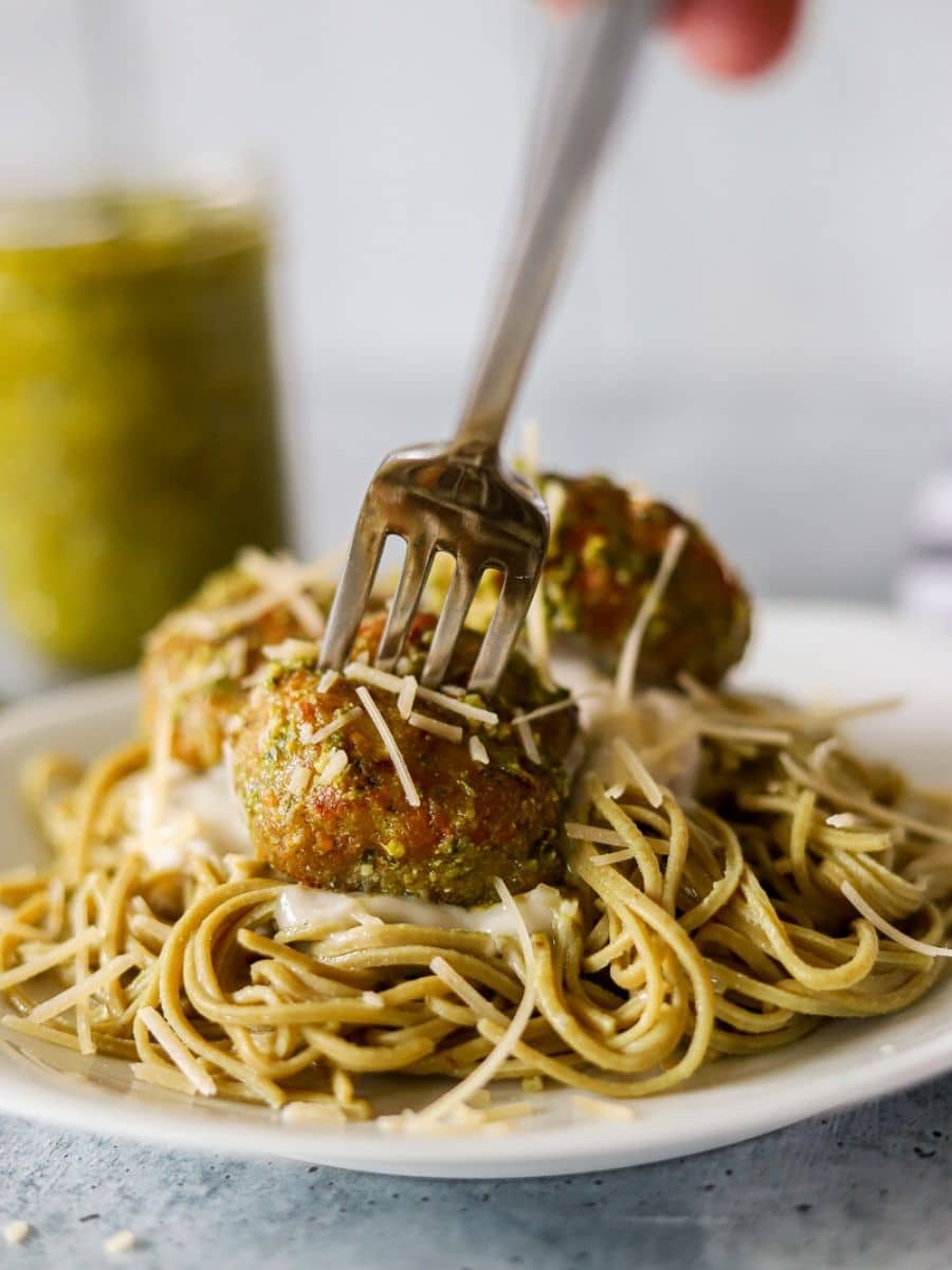 edamame pasta on a white plate toped with alfredo sauce and chicken pesto meatballs with text overlay