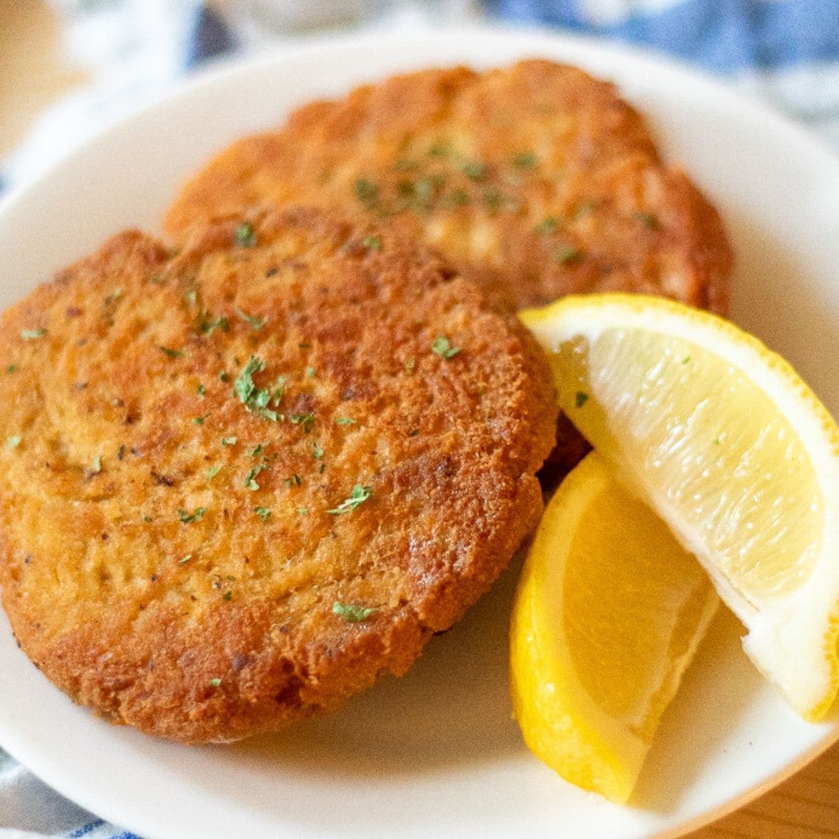 two salmon patties on a white plate garnished with lemon wedges and parsley