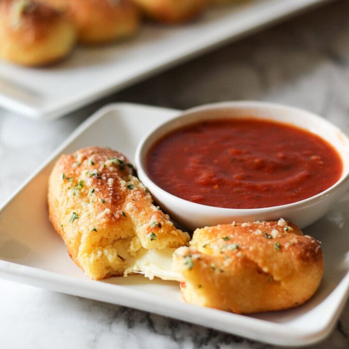 a pizza stuffed breadstick being torn in half with melted cheese coming from the center and a bowl of low carb marinara sauce off to the side.