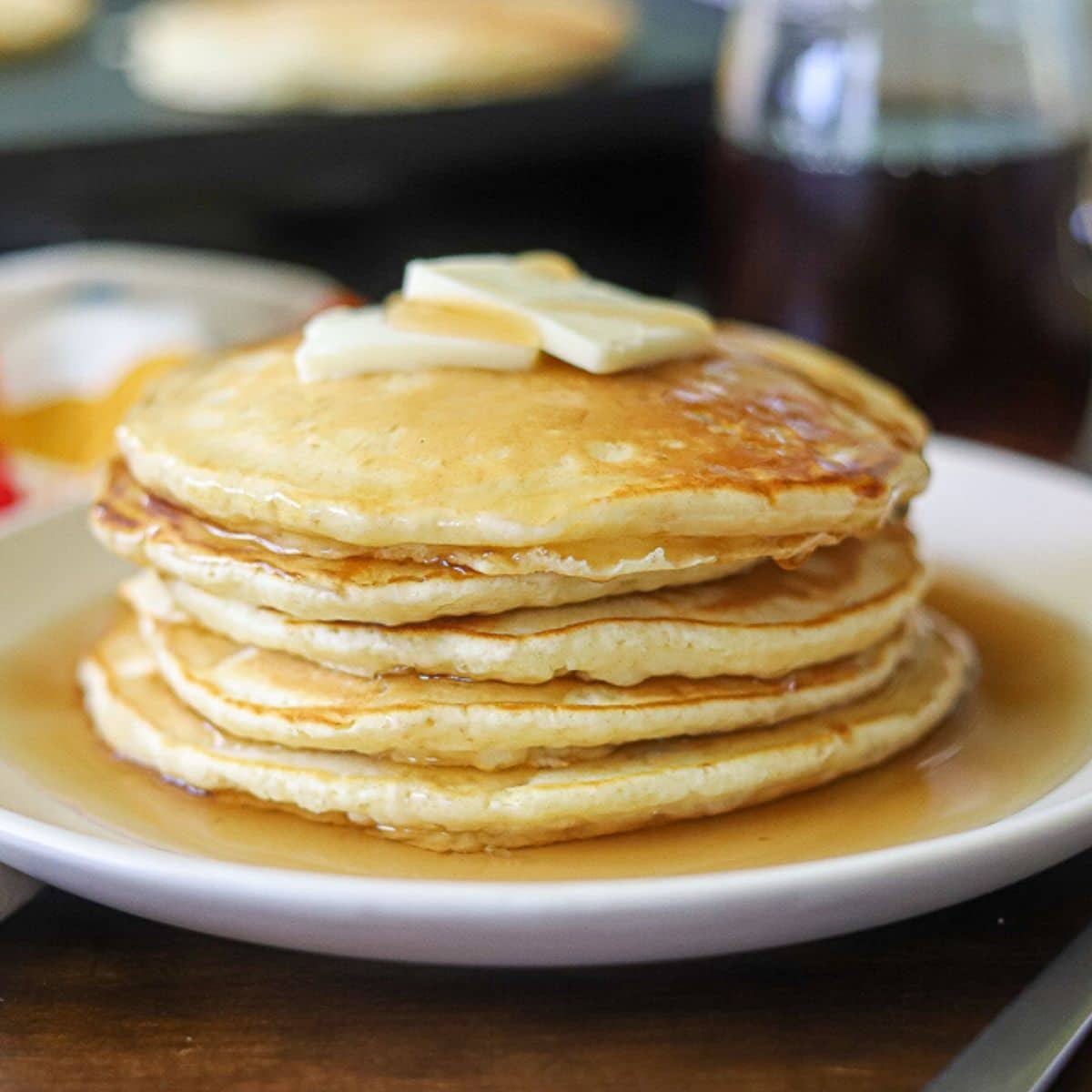 a side view of homemade pancakes stacked up on a plate topped with butter and syrup. 