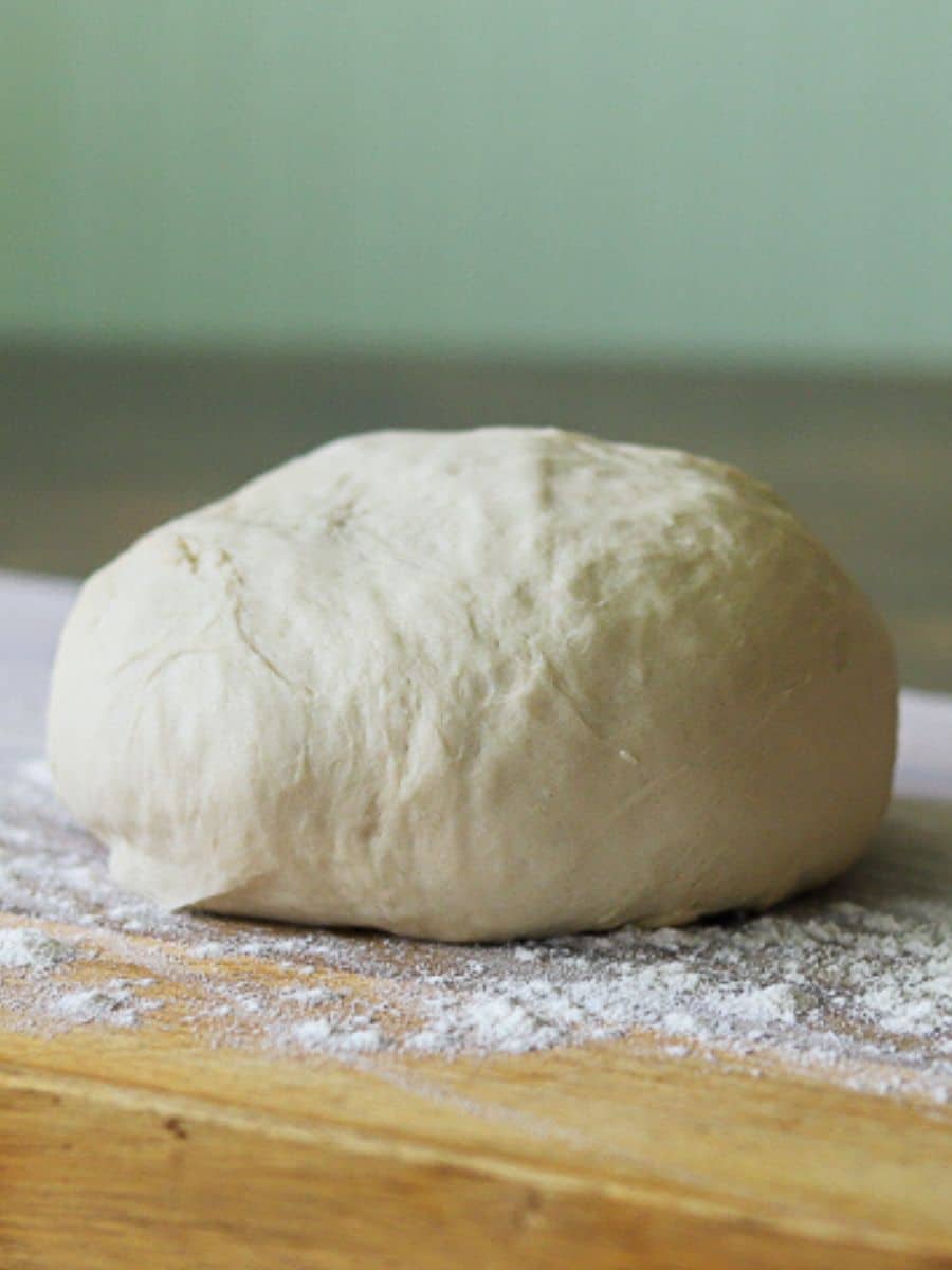 a ball of pizza dough on a floured wooden cutting board
