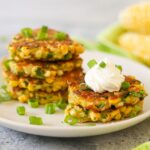 a plate full of golden Thai Corn fritters topped with sour cream and fresh chopped green onions