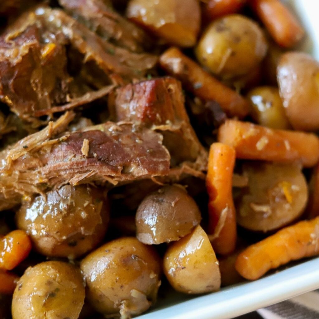 pot roast in a white pan with beef, carrots, and potatoes 