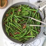 sautéed green beans in a skillet with crisp bacon and garlic.