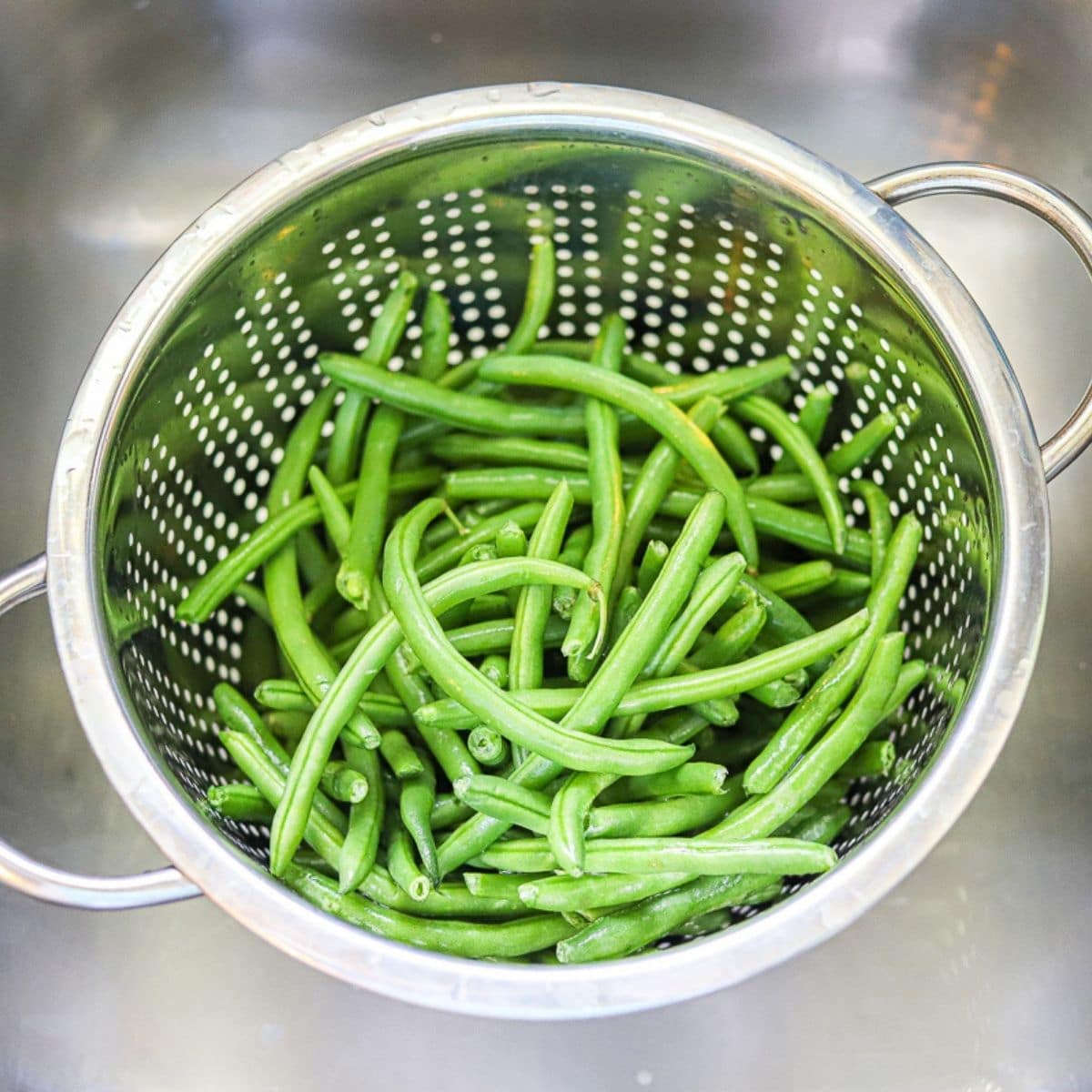 Fresh green beans in a silver colander in a sink.