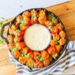 A ring of mini taco stuffed peppers in a cast iron skillet with a bowl of queso dip in the center